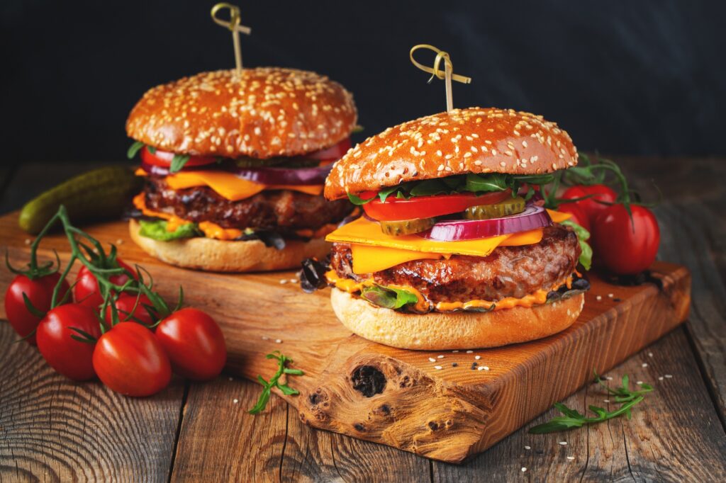 Two delicious homemade burgers of beef, cheese and vegetables on an old wooden table